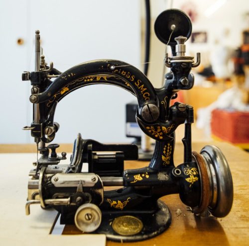 Antike Nähmaschine mit verzierten goldenen Details auf schwarzem Metallgehäuse in einem Innenraum.