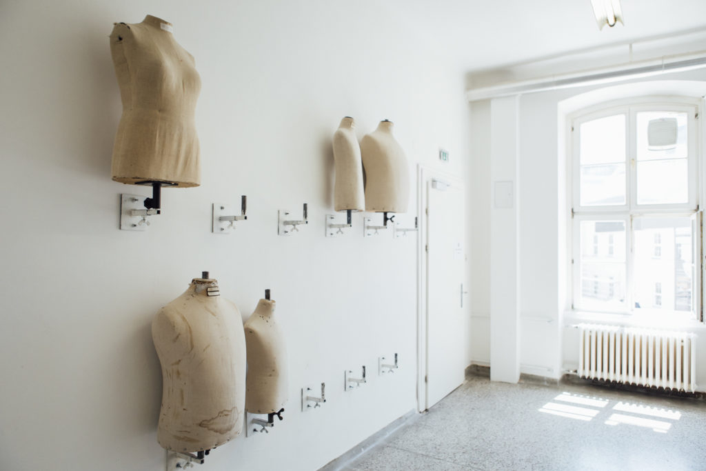 Mehrere Schneiderpuppen aus Stoff sind an einer weißen Wand in einem hellen Raum neben einem Fenster befestigt.