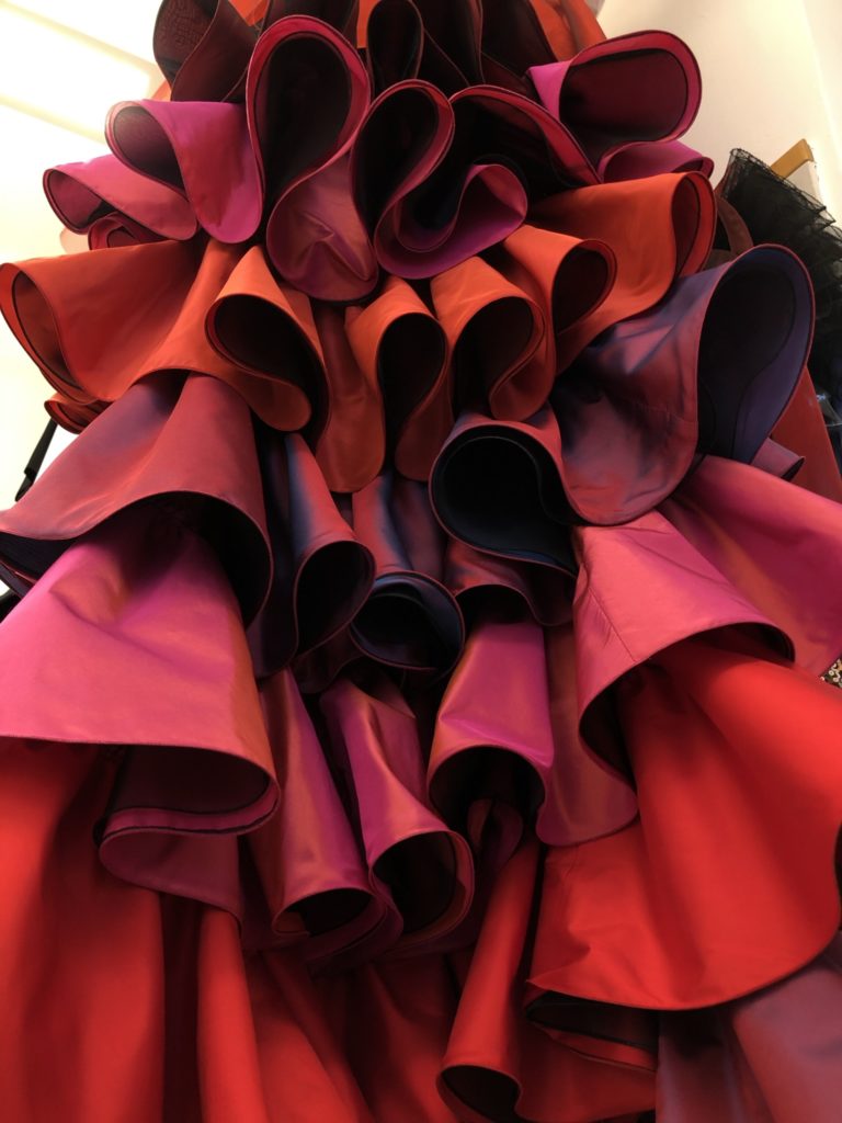 Multi-layered fabric in shades of red and pink, skilfully draped and arranged in curved, voluminous folds.