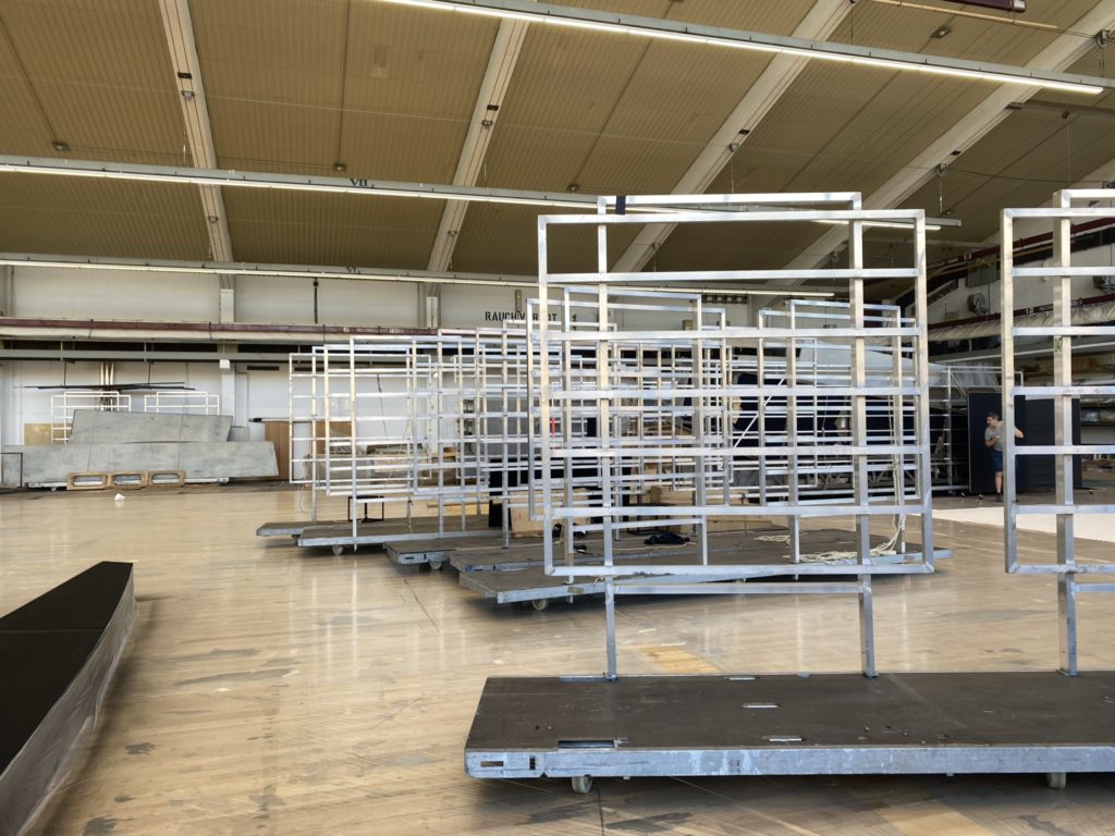 Mehrere metallene Gerüststrukturen auf Rollplattformen stehen nebeneinander in einer großen Halle mit hoher Decke.