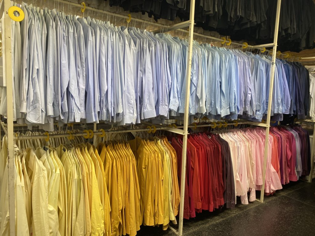 Viele ordentlich aufgehängte Hemden in verschiedenen Farben, von Gelb über Blau bis Rot und Rosa, in einem Bekleidungsgeschäft.