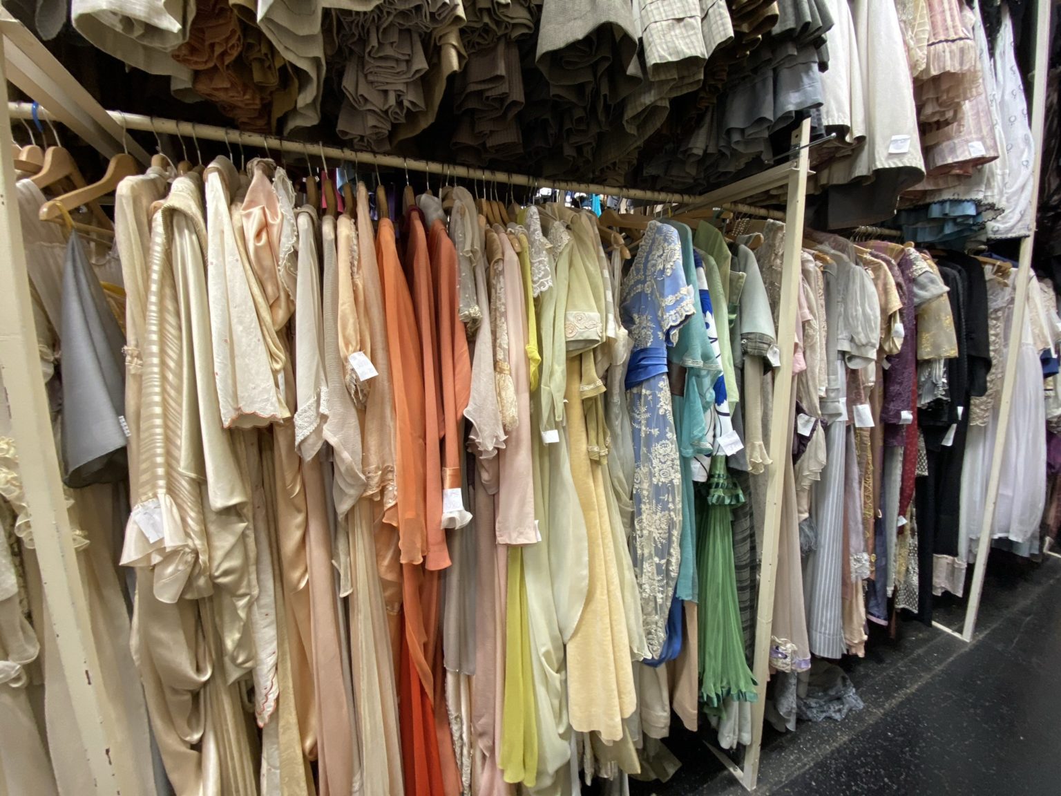 A row of elegant dresses in various pastel colours hangs neatly on hangers in a wardrobe.