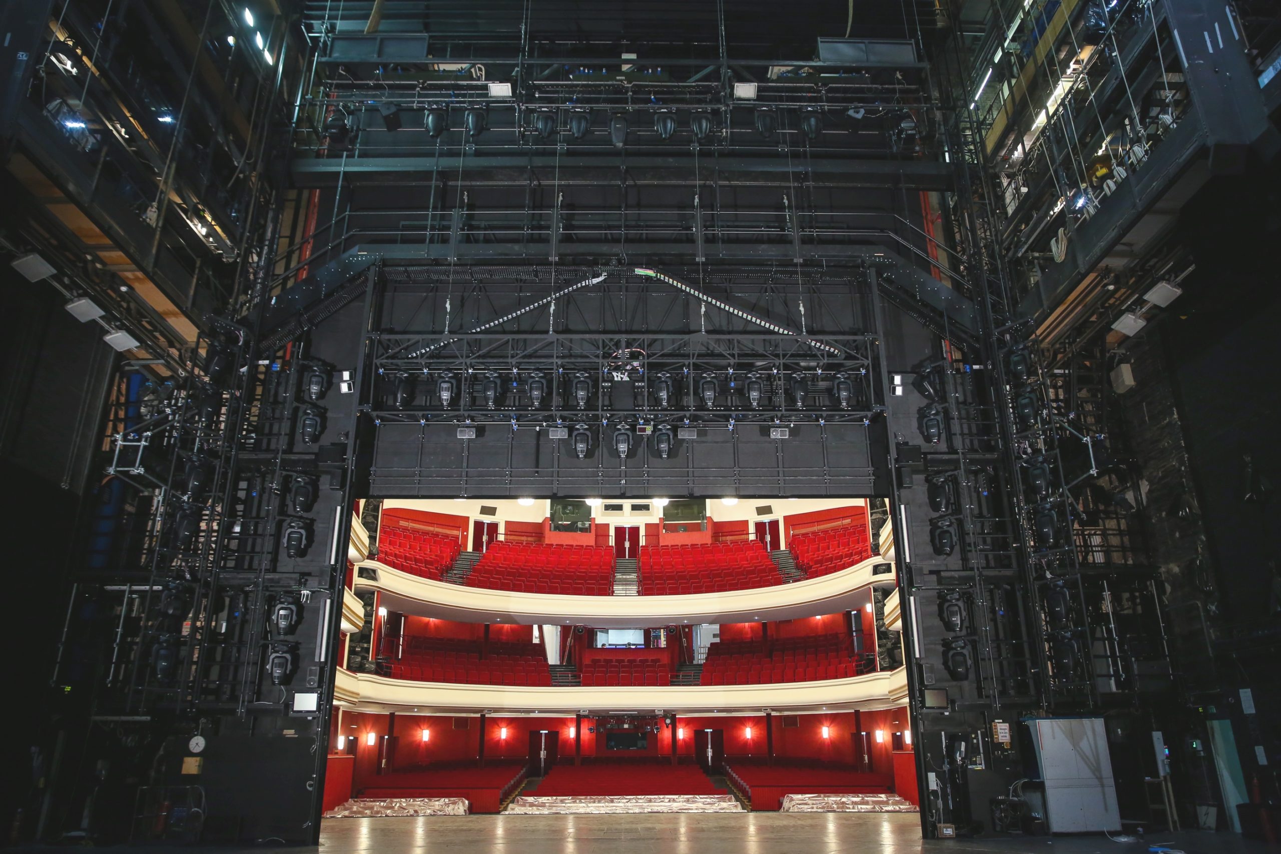 Die Bühne der Volksoper Wien von hinten gesehen. Man sieht das sogenannte Portal, in schwarz gehalten, in dem Beleuchtungsteile, Hubzüge, etc. verbaut sind. In der Mitte sieht man in den Besucherraum mit seinen roten samtbezogenen Sitzen. 
