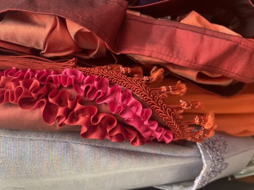 Mehrere Stoffe in Orangetönen und Lila mit Rüschen und Fransen liegen übereinander.