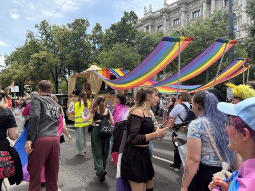 Menschen nehmen an einer bunten Pride-Parade teil, umgeben von Regenbogenflaggen und feierlicher Atmosphäre.