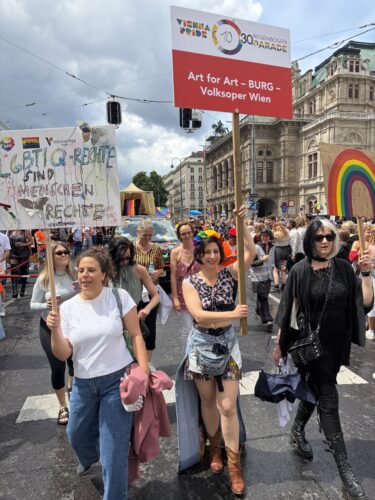 Menschen nehmen an einer Pride-Parade teil, halten bunte Schilder und Regenbogenflaggen, um für LGBTIQ-Rechte zu demonstrieren.